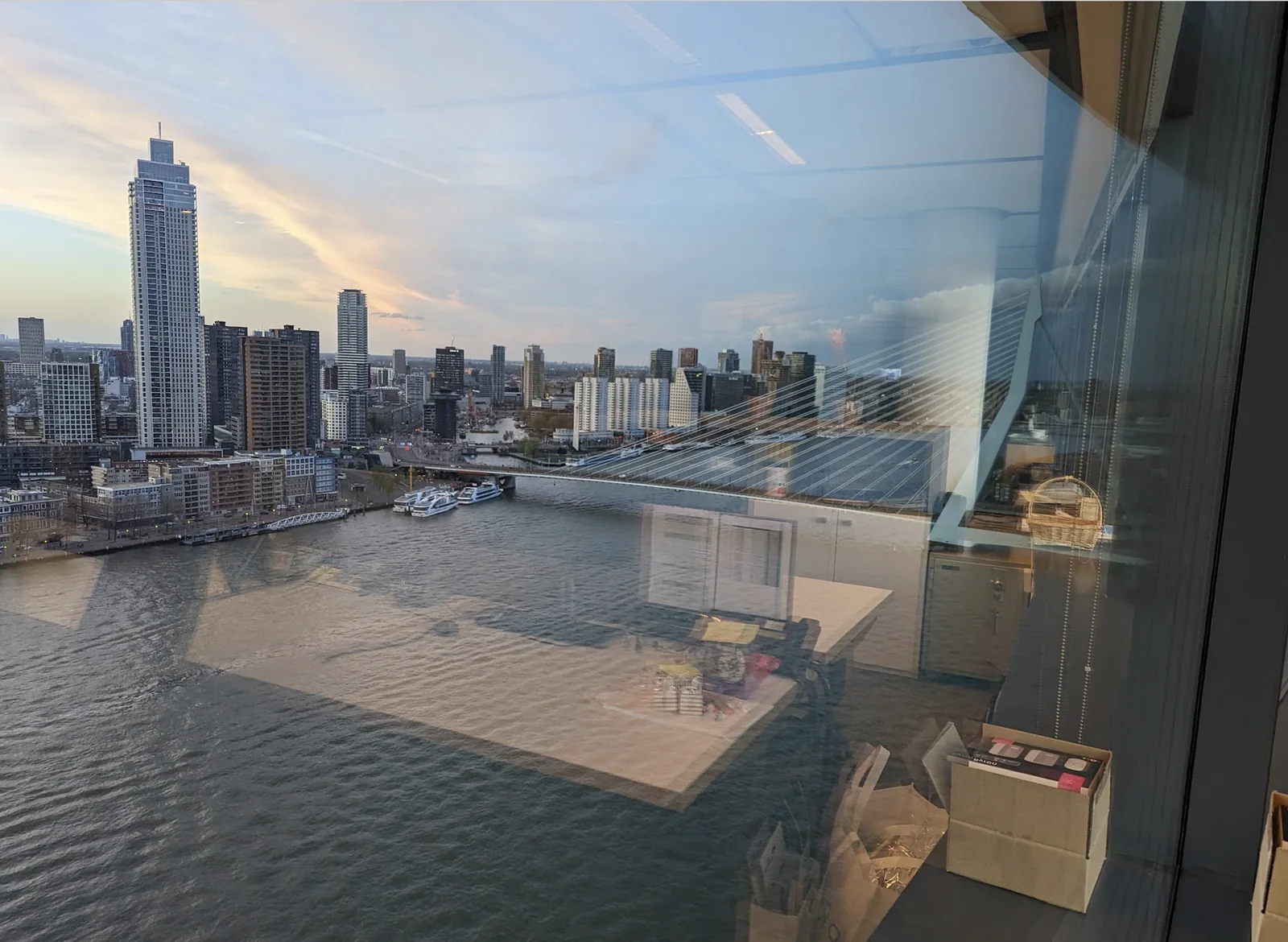De skyline van Rotterdam en de Maas bij zonsondergang, gezien vanaf een hoge verdieping.