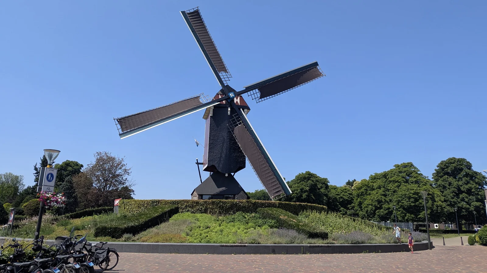 Een traditionele standerdmolen op een dorpsplein in Brabant, onder een strakblauwe lucht.